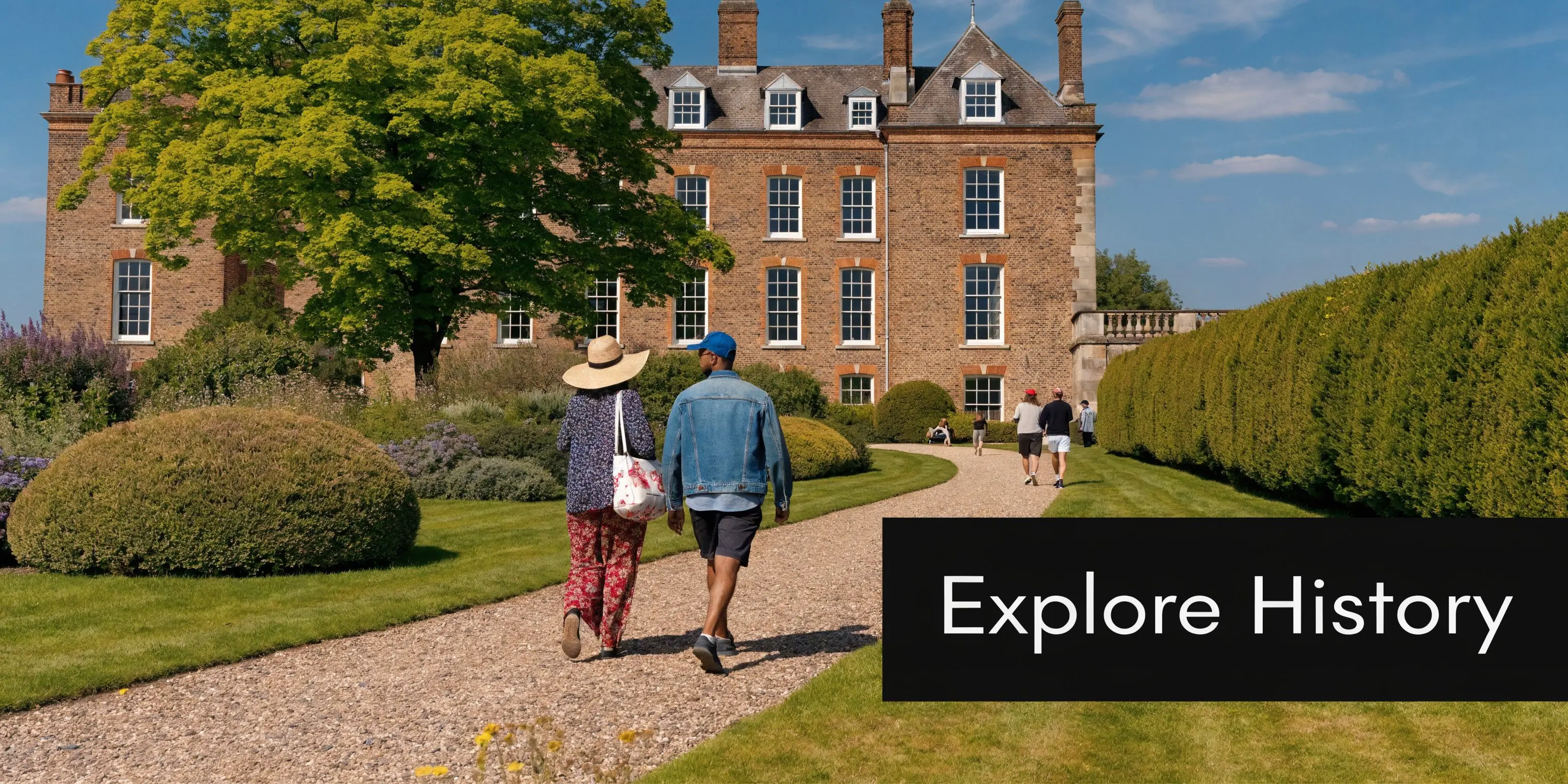 Visitors walking along a gravel path towards the historic Fulham Palace building in London on a sunny day.