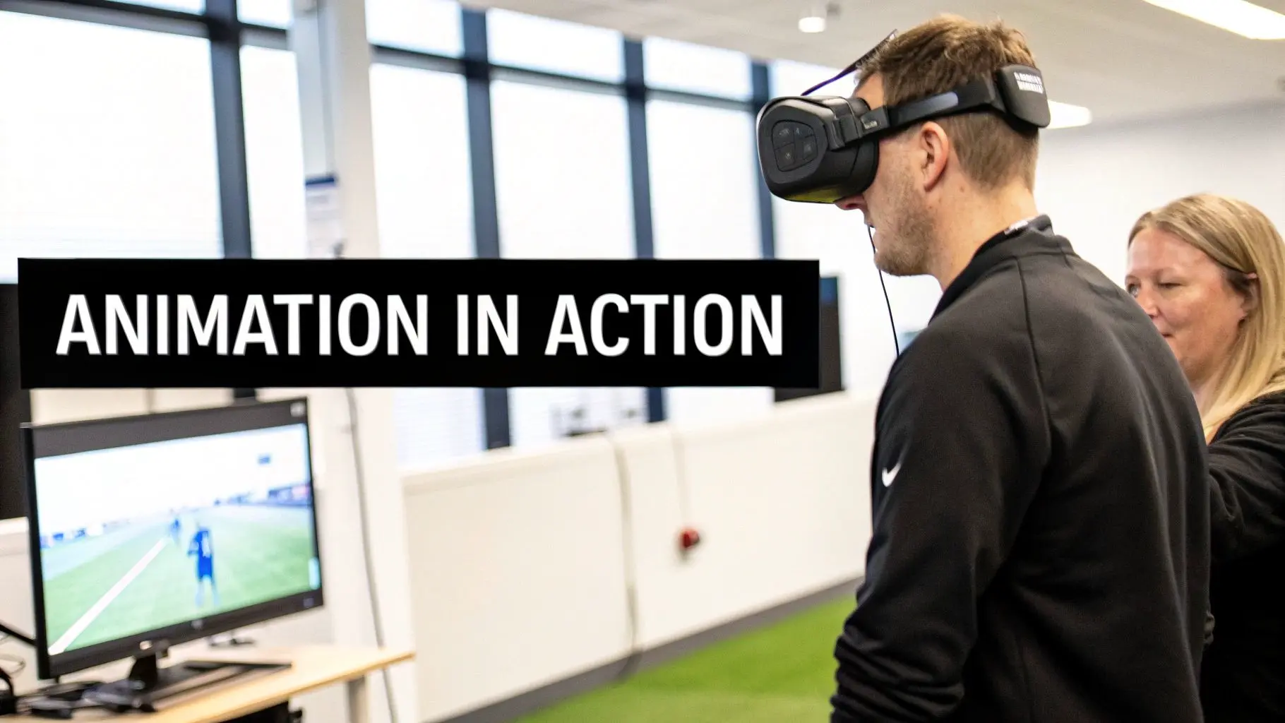 A man in a VR headset views a soccer animation on screen while a woman watches.