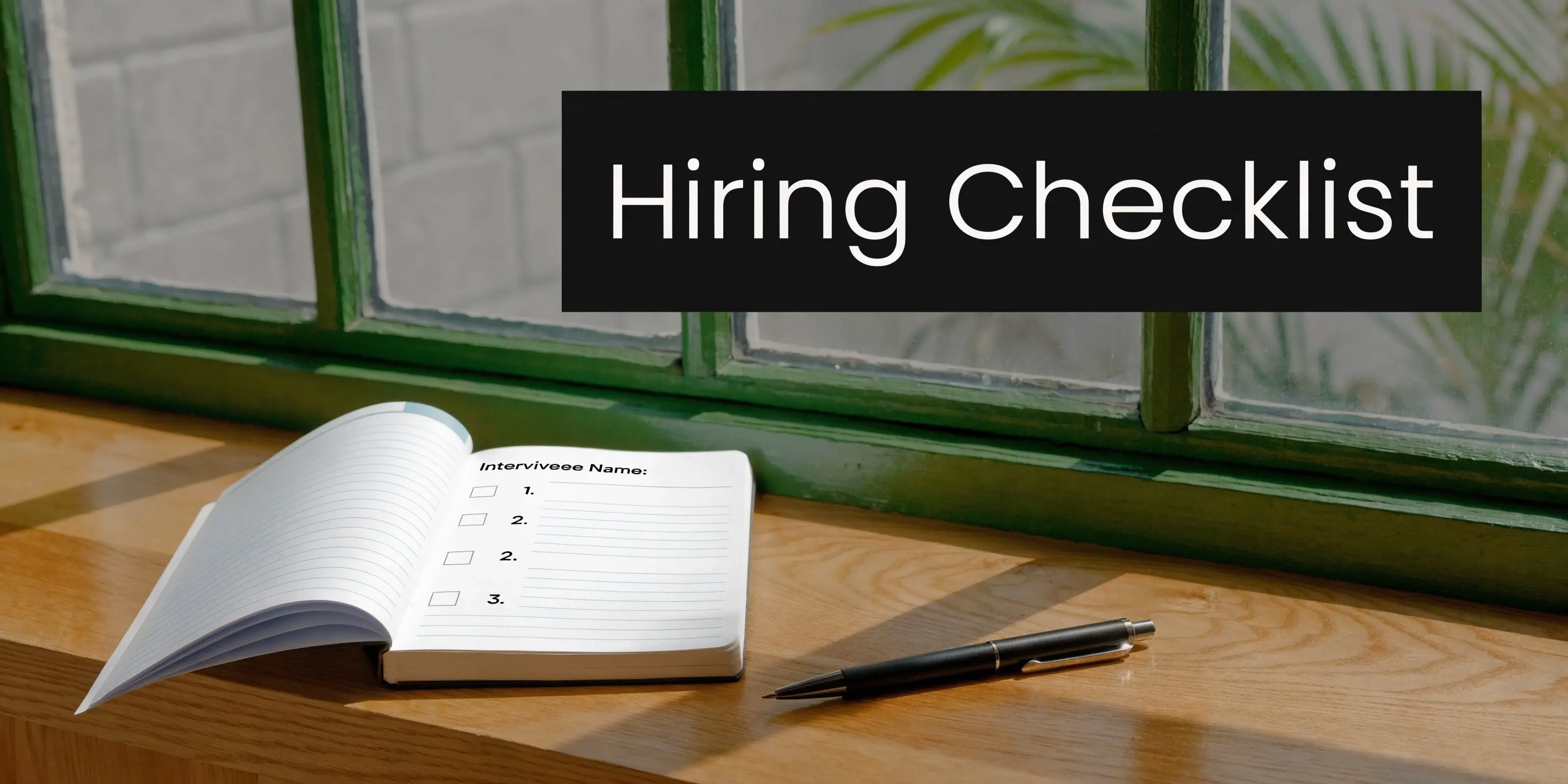 A hiring checklist journal with checkboxes sits on a wooden windowsill next to a black pen.