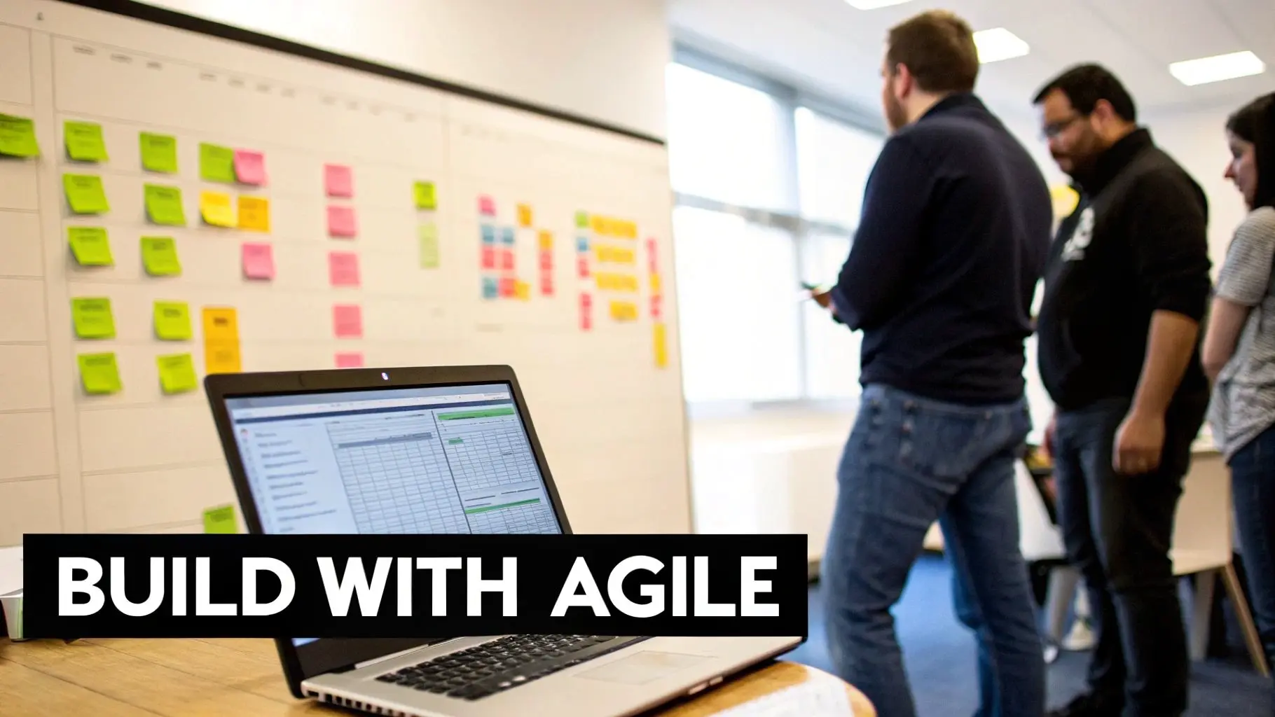 Diverse team collaborating on a whiteboard with colorful sticky notes, a laptop, and 'BUILD WITH AGILE' text.