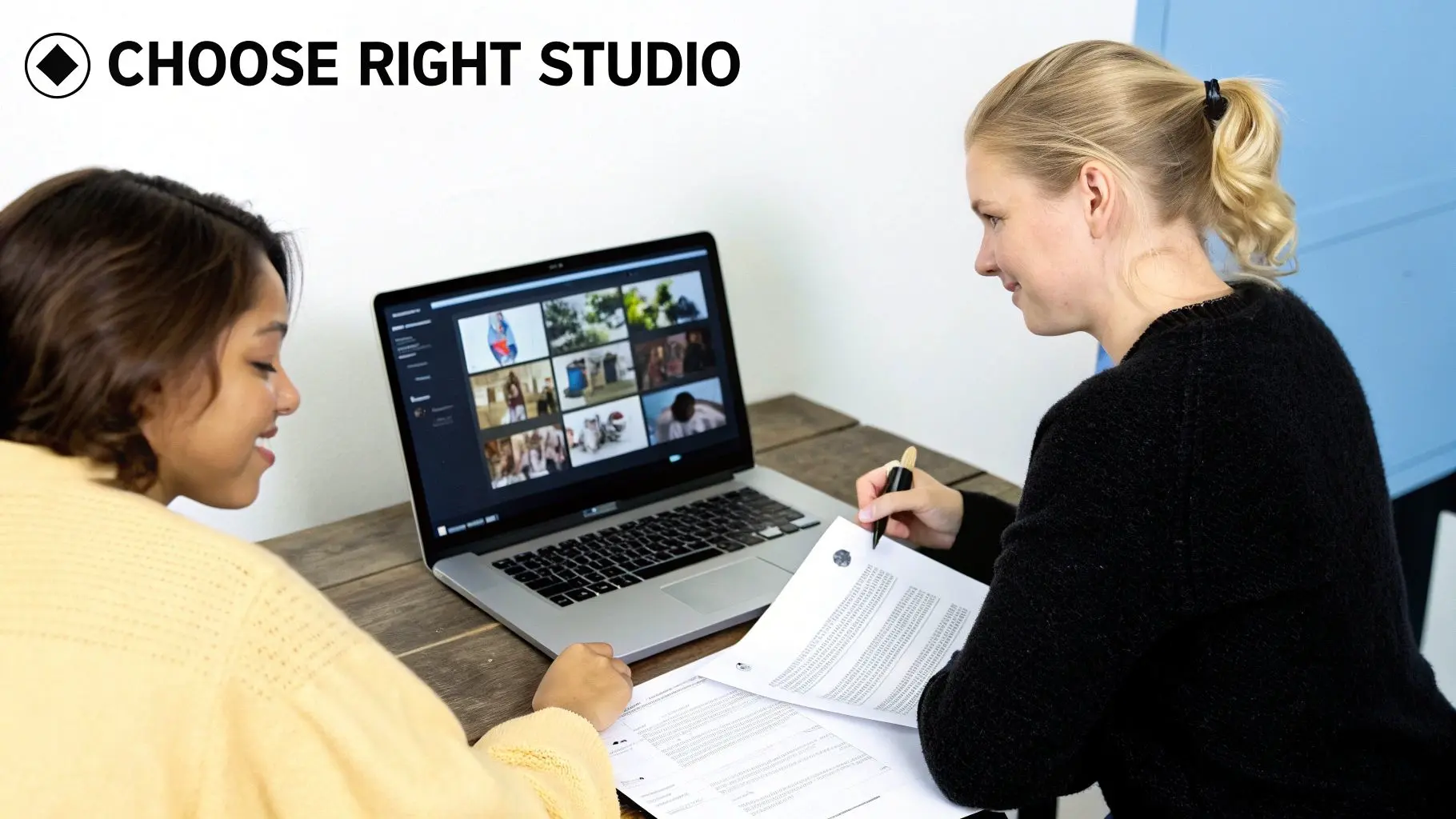 Two women review a laptop portfolio and documents, smiling and discussing options at a table.