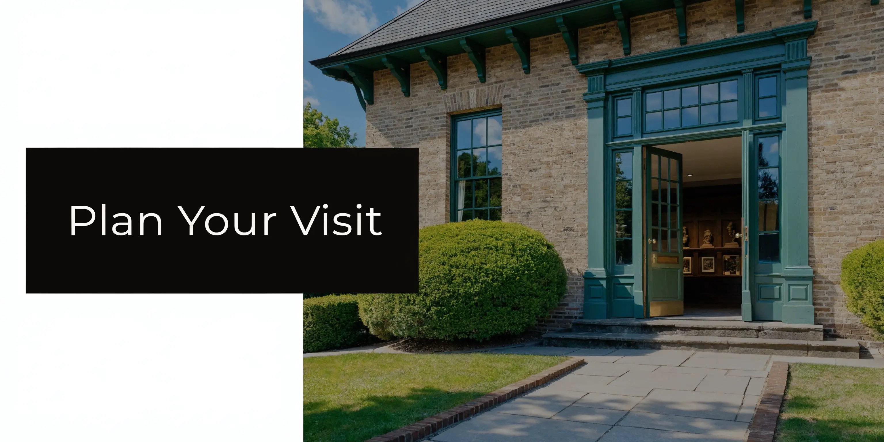 A historic brick building with green trim and an open entrance surrounded by lush green landscaping.