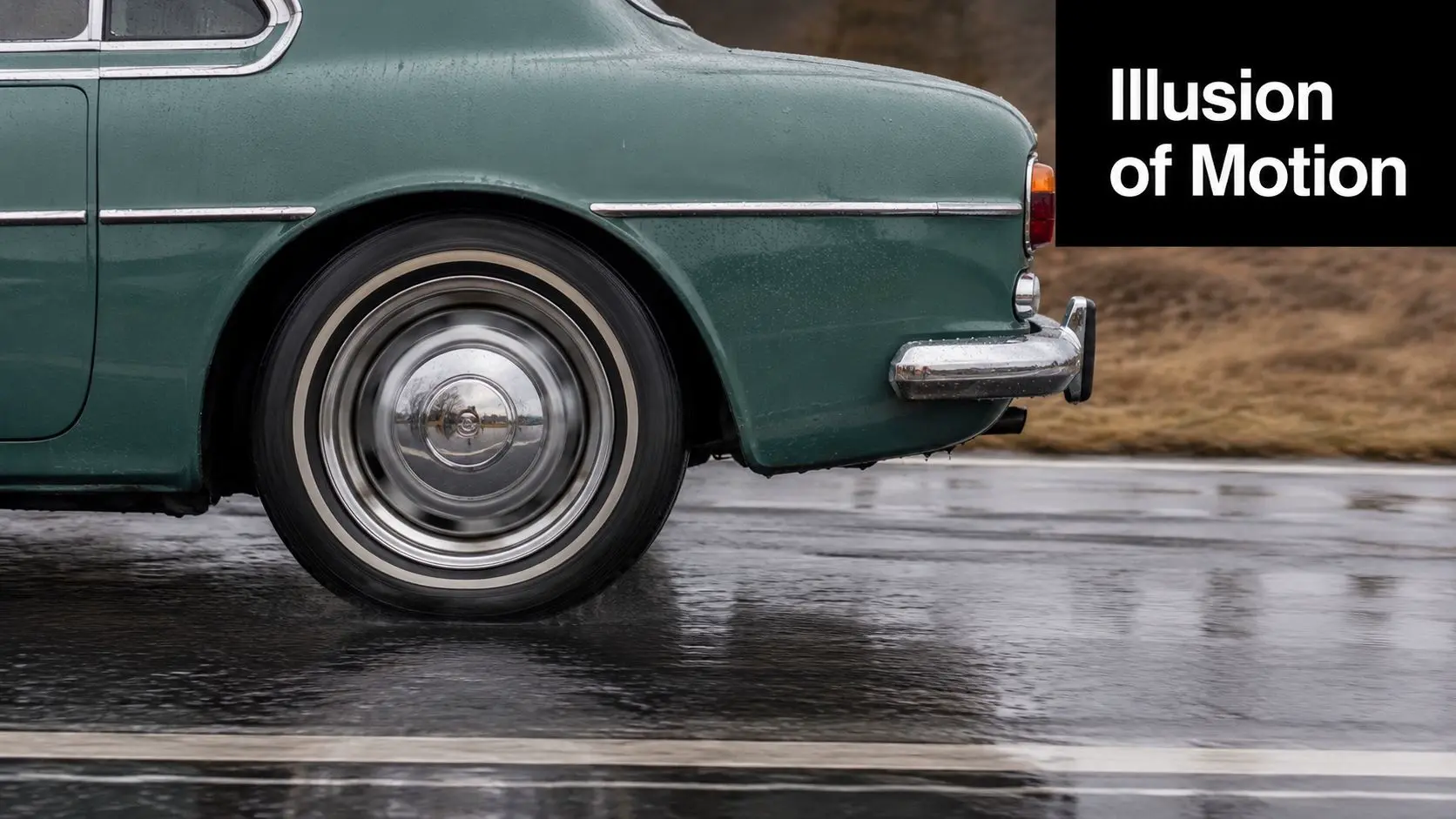 A close-up view of a vintage green car wheel displaying motion blur on a rainy road.