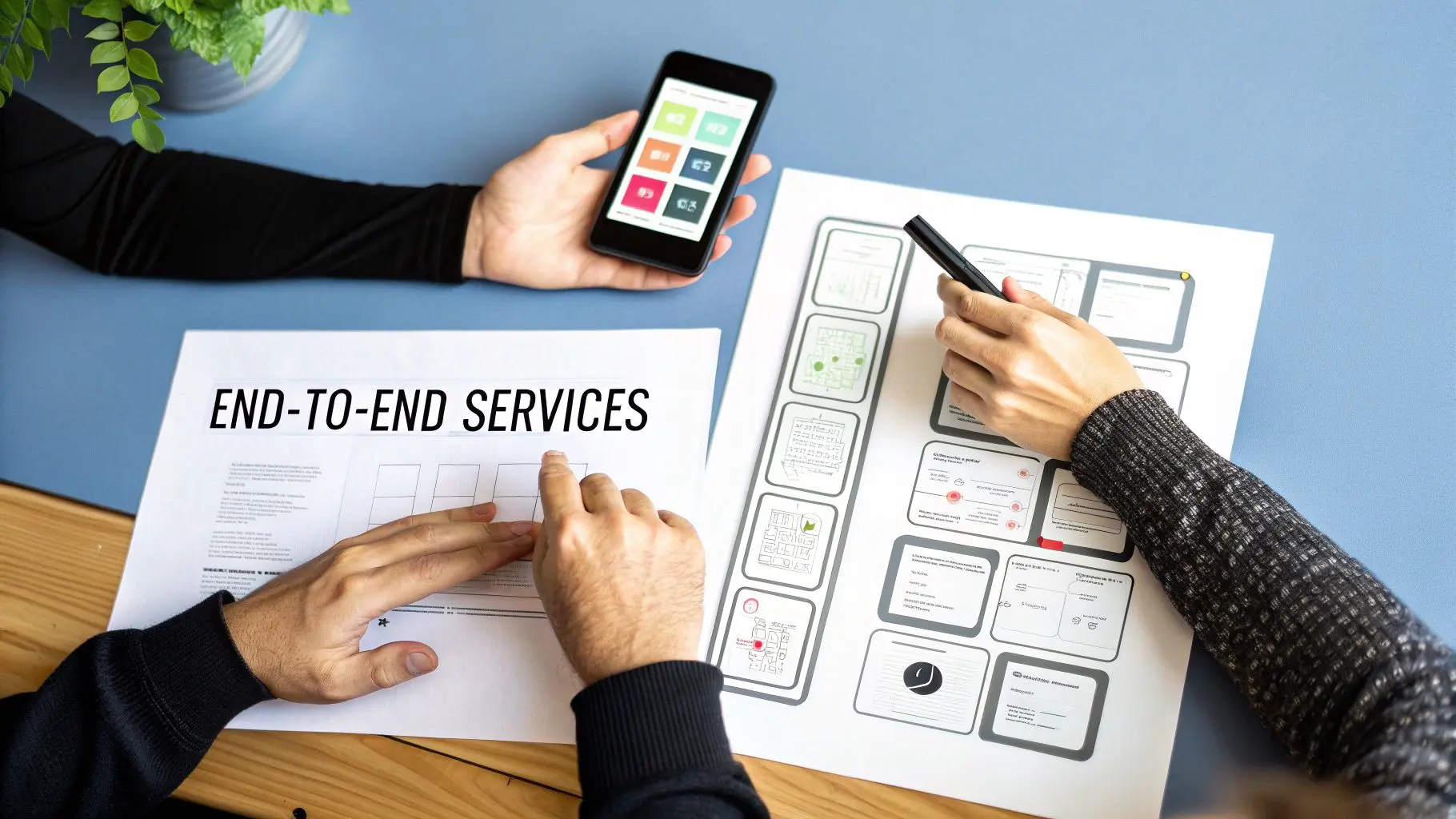 Three people collaborate on app development, reviewing wireframes and a mobile app interface on a blue table.